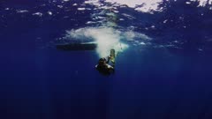 Underwater view of small boat at surface of blue Pacific Ocean, then a person enters the water, and swims toward camera. (Human has fins and snorkel and wet suit).  Pretty ocean surface, reflective, mirror like, seen from below. This good long footage cuts with the RARE footage of a blue whale (Balaenoptera musculus) with a human swimmer, good perspective of size of the whale.  Near San Diego, California, in summer when blue whales (Balaenoptera musculus musculus) are attracted by krill (Euphausia pacifica), see few tiny pink bits passing by camera in upper corners where krill catch the light. The water has particles in it, this is the krill or plankton. Healthy Ocean. North America West Coast.