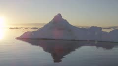 POV, on water passing icebergs, sun setting with sunrays