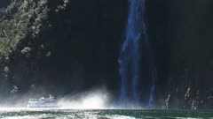 a cruise boat sails into the spray at the base of stirling falls in milford sound, new zealand