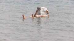 a man floats in the incredibly salty dead sea of israel and reads a newspaper
