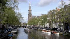 a tour boat on a canal with westerkerk in the distance at amsterdam, netherlands
