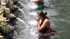 a female tourist submerges under a holy water fountain at tirta empul temple on bali, indonesia