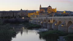 a dusk wide angle zoom in clip of the ancient roman bridge and the mosque-cathedral of cordoba, spain