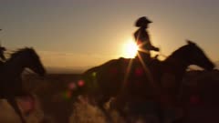 Slow motion shot of cowboys galoping at sunset.