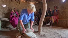 tourist grind flour on a stone with group of women of Datoga tribe, Lake Eyasi, Tanzania, Africa