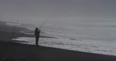 A Fisherman in silhouette on a mist shrouded and dramatic Pacific Ocean beach rocked with heavy surf and powerful waves by the forces of the 2016  El Niño