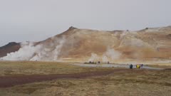 Geothermal area in North Iceland, steam rising. tourists walk towards lens in distance