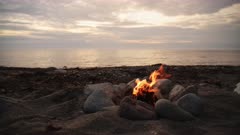 Wild camping on the beach - Small campfire bonfire surrounded by rocks on shore in Wales during outdoor adventure camping trip