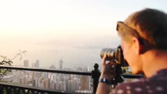 Man Holding A Camera Taking Photos Of The Beautiful Hong Kong City Skyline With Ships Sailing Across The Open Ocean On A Bright Morning Sky - Closeup Shot