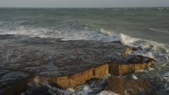 Waves crashing on the cliffy shoreline in Portland, England, on a cloudy evening