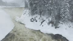 Spectacular winter wonderland scene filmed by drone flying over flowing river