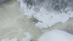 Strong water current of a river's cascade going thru icy snow piles in the wild