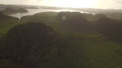 Aerial view over jungle covered hills and water at sunset