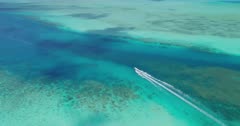 Aerial shot following speed boat along channel tilting up to reveal tropical islands