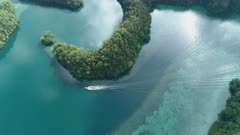 Aerial shot of Palau Rock islands on very calm morning with calm water reflecting sky as boat travels between islands creating wakes in mirroring water 