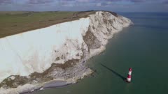 Aerial shot flying along high white cliffs towards lighthouse in the sea