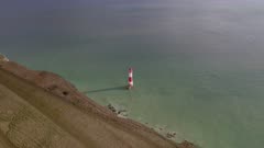 Aerial shot flying over the edge of a high sea cliff down towards a lighthouse 
