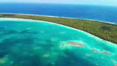 Aerial shot flying over turquoise lagoon towards atoll in tropical Pacific