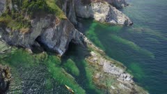 Aerial drone shot looking down on coastal cliffs and submerged rock formations as kayakers paddle through the frame