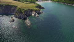 Aerial drone shot flying down towards coastal cliffs and submerged rock formations with group of kayakers