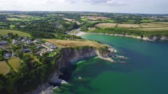 Aerial drone shot flying down towards coastal cliffs beach filled with tourists, Summer, Cornwall, UK