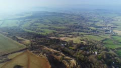 High aerial shot flying above Neolithic Hillfort and Barrow on top of Leckhampton Hill in Gloucestershire, UK