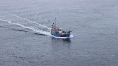 Telephoto shot of small fishing trawler traversing diagonally through frame on calm grey ocean, exits frame. Cornwall, UK.