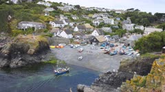 Wide shot of small fishing trawler approaching a sheltered cove and fishing village. Beaches itself. Cornwall, UK.