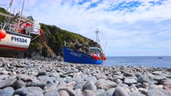 Wide shot of fishing trawler resting on a stony beach in summer, Cornwall, UK