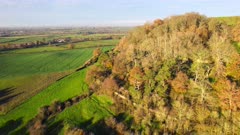 High wide shot flying ramparts of Cadbury Hillfort towards fields in Somerset. UK on cold winter afternoon