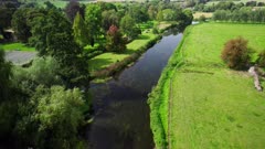 Aerial shot tracking along the River Avon as it flows through a small village in Wiltshire, UK