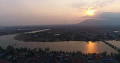 Drone footage of the south-west area of Kampot city, Cambodia. The camera is going sideways showing the western part of Kampot and the Praek Tuek Chhu river before it splits in 2 to create fish island. You can see the Bokor National Park Hills in the background where the sun is setting.