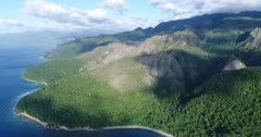 Drone footage of Wetar island with its luxuriant tropical vegetation and rocky hills. The camera is facing the island and is going towards the rocky hills inland.
