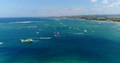 Drone footage of parasailing and other water activities in front of Benoa bay in Nusa Dua. The camera is facing the boats in front of Tanjung Benoa beach and Nusa Dua and is going backward towards Serangan over the water while descending, ending up over the green water of the pond.