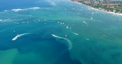Drone footage of parasailing boats in the south of Serangan island just opposite to Benoa bay. The camera is facing down at 2 boats towing their parasail and is panning to follow them.