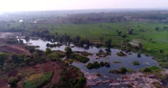 Drone footage of countryside near Mysore, Karnataka, India, with the rocky bed of the Kaveri river, one of its side pretty dry with red earth and the other one with bright green rice fields at various stage. The camera is doing a full 360 degrees panning of the area.