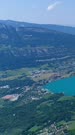 Vertical drone footage of the Annecy lake and the surrounding mountains with dense forest over it. The camera is starting facing the Annecy lake and is going sideways behind the mountain.