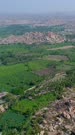 Vertical drone footage of the countryside near Hampi, Karnataka, India, with its rocky landscape and the granite like boulders forming hills with fields in between. The camera is going towards a hill while descending.