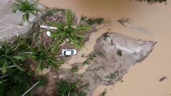 Aerial top down view car is flush away during flash flood and trap near the coconut tree