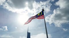 Aerial tracking Malaysia flag at Dataran Merdeka with background of PNB118 tower in blue sunny sky