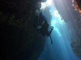 Diver Swims Through Crevice Or Cave, Lit By Sun Rays
