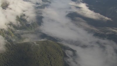 High angle view of mountains and clouds below, pan and tilt left to mountains in distance, cam approaches mountains