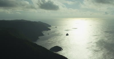 Circling island coast silhouette, slight pan to horizon with cloud shadows on water.