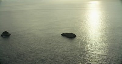 zooming in towards rock on ocean, reflected sun on water