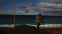 Man Films With Video Camera On Beach Near Wind Sock