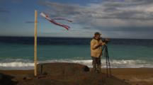 Man Films With Video Camera On Beach Near Wind Sock