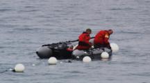 Men Wearing Exposure Suits In Inflatable Boat Pull On Net With Buoys