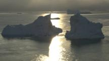 Icebergs Silhouetted By Sunset Or Sunrise Reflected On Ocean