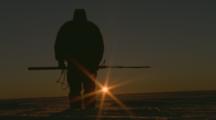 Inuit Man Stands On Ice, Flare Of Sunrise Behind 