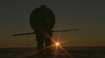 Inuit Man Stands On Ice, Flare Of Sunrise Behind 